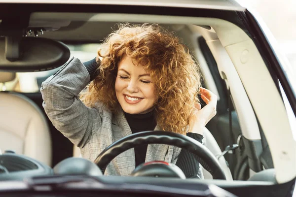 Feliz hermosa jengibre rizado mujer con los ojos cerrados sentado en el coche - foto de stock