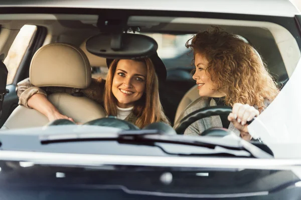 Smiling redhead woman driving car while her female friend sitting on backseat — Stock Photo