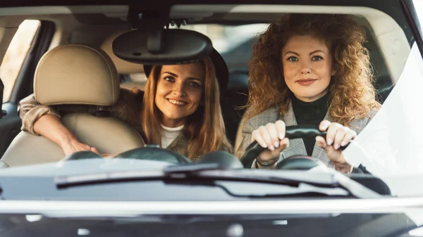 Curly ginger woman driving car while her smiling female friend sitting on backseat — Stock Photo