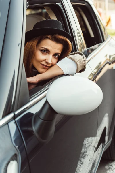 Beautiful woman in black hat sitting in car at urban street — Stock Photo