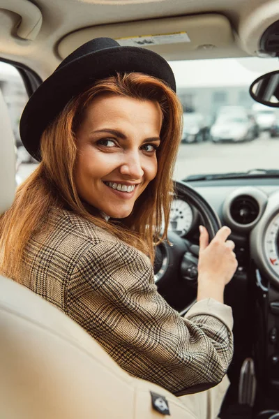 Портрет улыбающейся женщины в черной шляпе и клетчатой куртке, сидящей за рулем в машине — стоковое фото