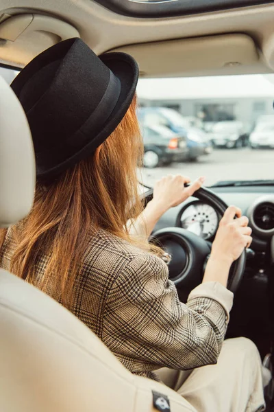 Vue arrière de la femme en chapeau noir et veste à carreaux assis au volant dans la voiture — Photo de stock