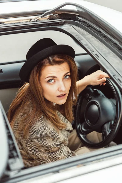 Vista de ángulo alto de la mujer en sombrero negro sentado al volante en el coche - foto de stock