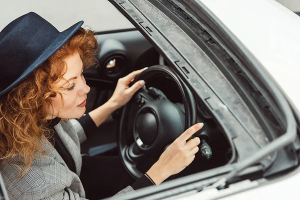 Vista ad alto angolo della donna alla moda in cappello nero e giacca grigia seduta al volante in auto — Foto stock