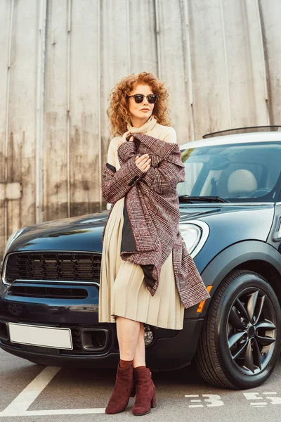 Stilvolle Ingwerfrau mit Sonnenbrille in der Nähe von Auto an der Stadtstraße — Stockfoto