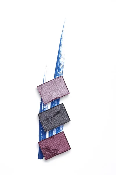 Disposición plana con sombras de ojos negro y púrpura sobre fondo blanco - foto de stock