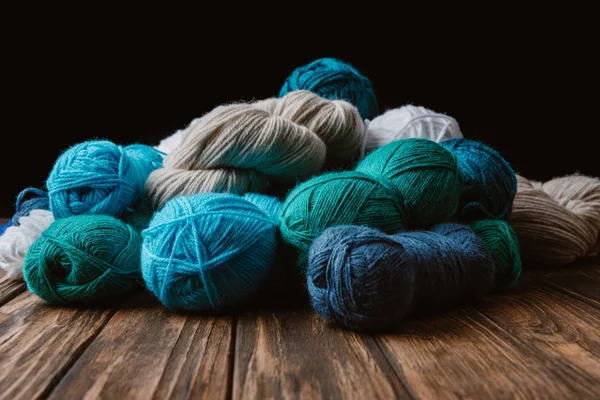 Close up view of white, blue and green yarn for knitting on wooden surface on black backdrop — Stock Photo