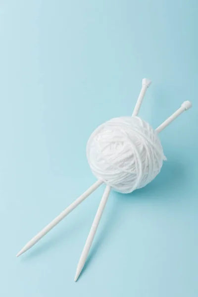 Close up view of white yarn ball and knitting needles on blue background — Stock Photo