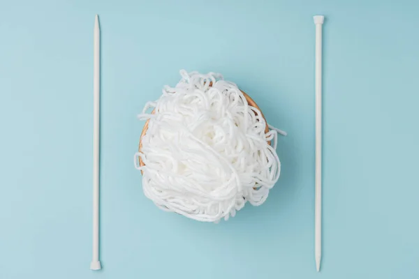 Top view of white yarn in bowl and knitting needles on blue backdrop — Stock Photo