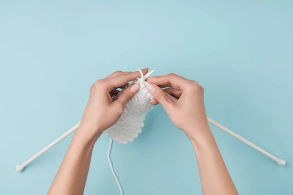 Partial view of woman with white yarn and knitting needles knitting on blue backdrop — Stock Photo