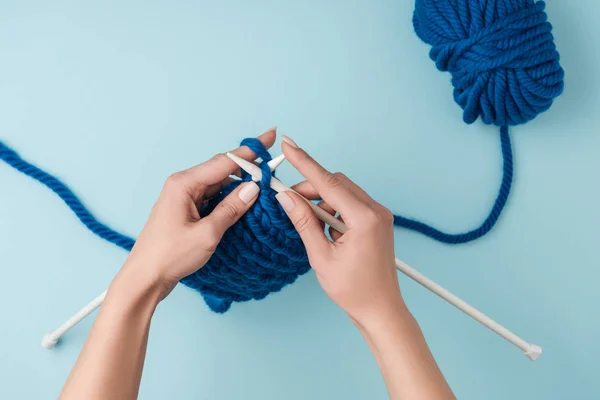 Tiro recortado de la mujer tejiendo sobre fondo azul con hilo azul - foto de stock