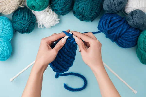 Cropped shot of woman knitting on blue background with blue, green and white yarn clews — Stock Photo