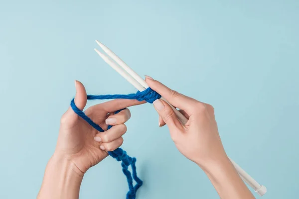 Vue partielle de la femme avec fil bleu et aiguilles à tricoter blanches tricotant sur fond bleu — Photo de stock