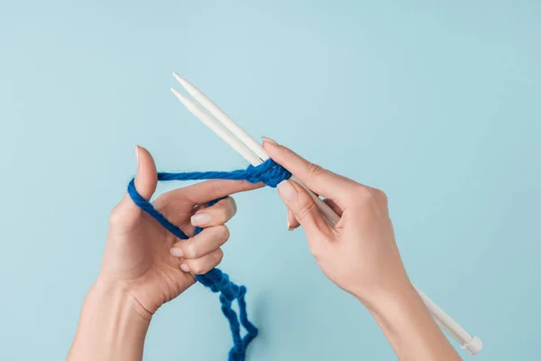 Visão parcial da mulher com fios azuis e agulhas de tricô branco tricô no fundo azul — Fotografia de Stock