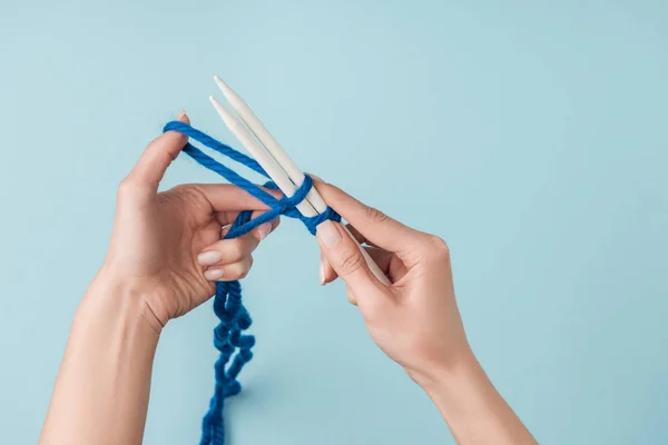 Teilansicht einer Frau mit blauem Garn und weißen Stricknadeln auf blauem Hintergrund — Stockfoto