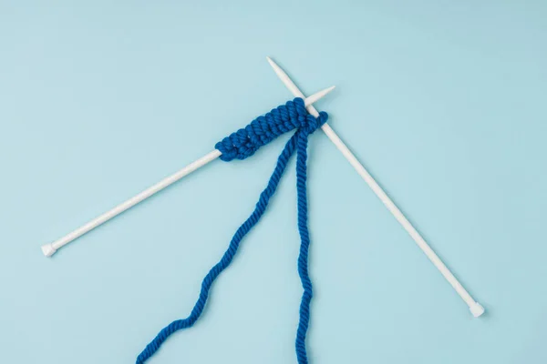 Vista superior de fios azuis e agulhas de tricô branco no fundo azul — Fotografia de Stock