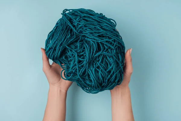 Vue partielle de la femme tenant du fil pour tricoter dans les mains sur fond bleu — Photo de stock