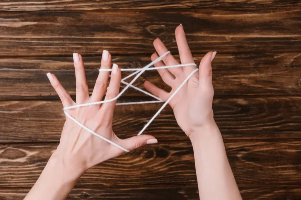 Vista parziale della donna che tiene il filato bianco per lavorare a maglia sulle mani su un tavolo di legno — Foto stock