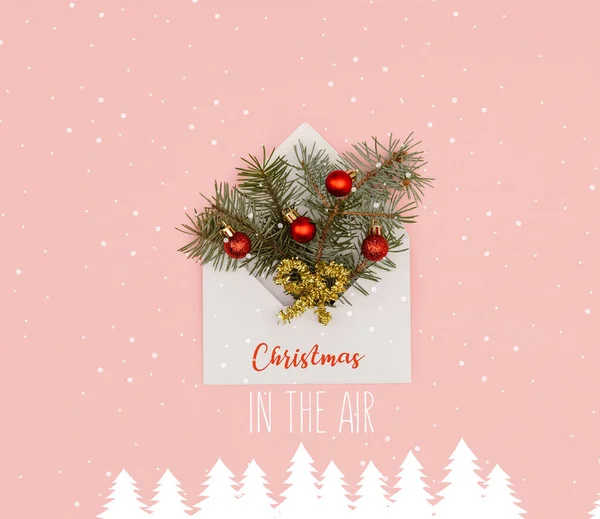 Vue de dessus de l'enveloppe blanche avec des brindilles de sapin et des boules de Noël brillantes isolées sur rose avec l'inspiration 