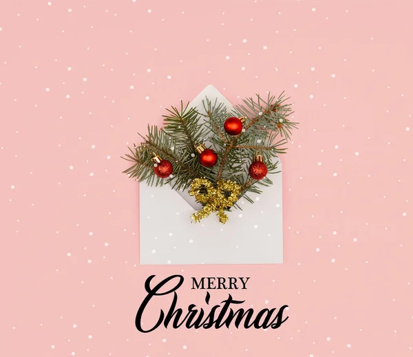 Vue de dessus de l'enveloppe blanche avec des brindilles de sapin et des boules de Noël brillantes isolées sur rose avec lettrage 
