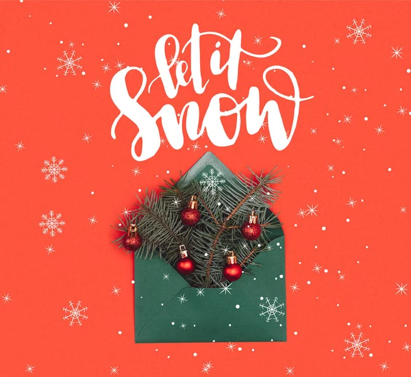 Close-up view of green envelope with fir twigs and shiny christmas baubles isolated on red with 