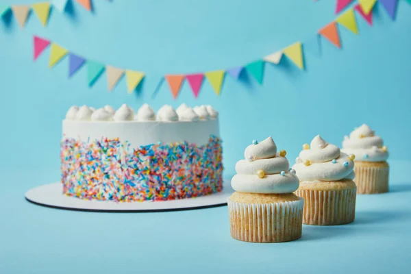 Deliciosos cupcakes e bolo com polvilhas de açúcar no fundo azul com bunting — Fotografia de Stock