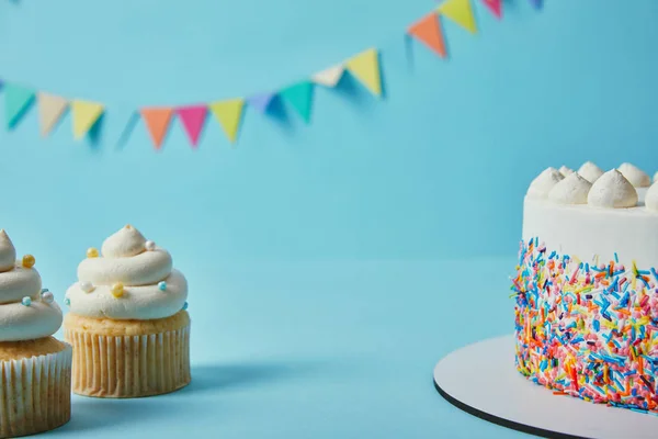 Sabrosos cupcakes y pastel sobre fondo azul con banderines - foto de stock