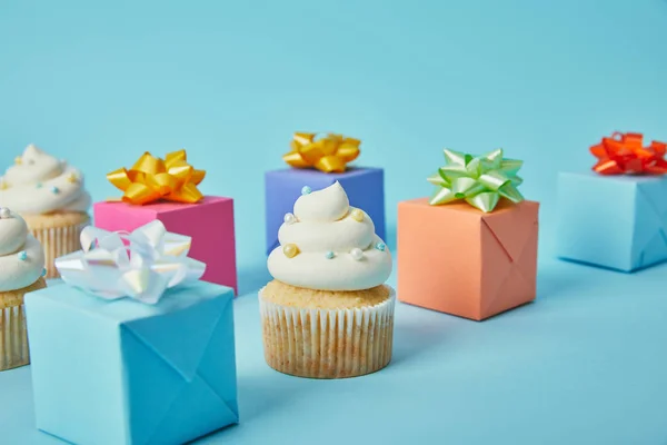 Délicieux cupcakes et cadeaux colorés sur fond bleu — Photo de stock
