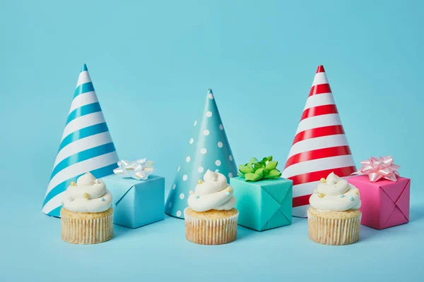 Bonés de festa coloridos, presentes e cupcakes saborosos no fundo azul — Fotografia de Stock