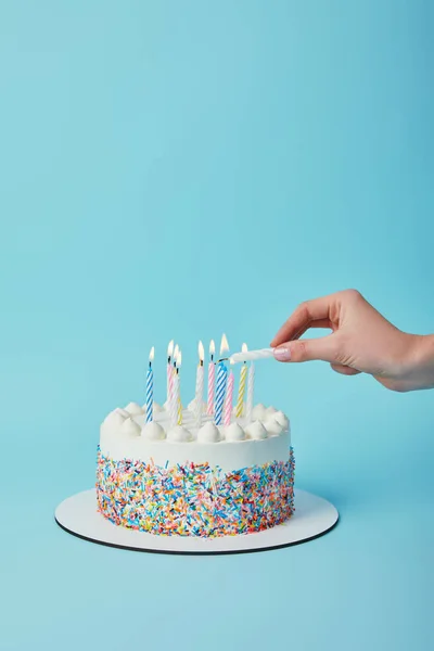 Partial view of woman lighting candles on birthday cake on blue background — Stock Photo