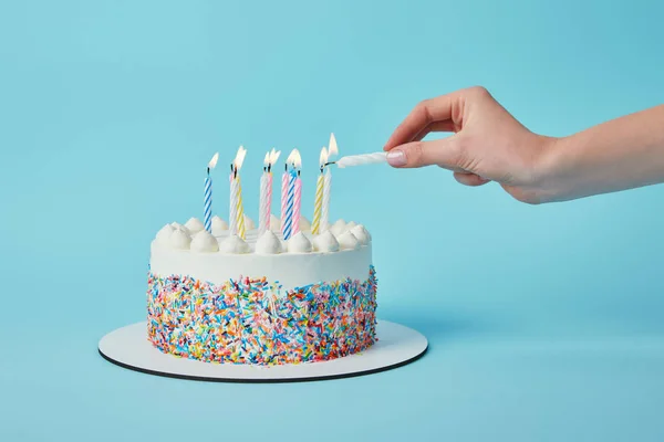 Partial view of woman lighting candles on birthday cake on blue background — Stock Photo