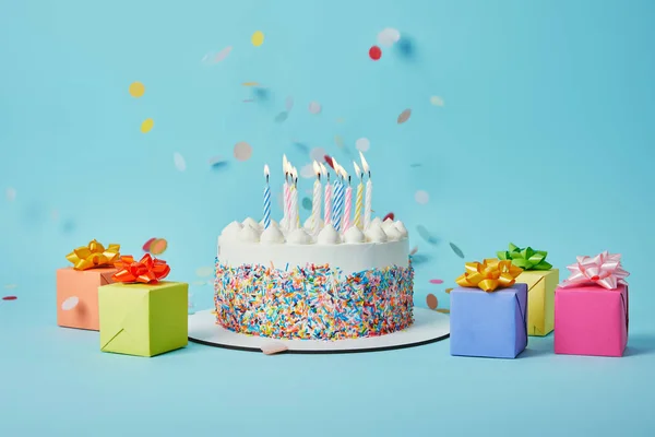 Gâteau savoureux aux bougies, cadeaux colorés et confettis sur fond bleu — Photo de stock