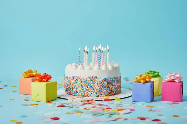 Delicious cake with candles, colorful gifts and confetti on blue background — Stock Photo