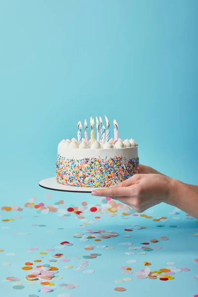 Vista cortada de mulher segurando delicioso bolo de aniversário com velas no fundo azul com confete — Fotografia de Stock