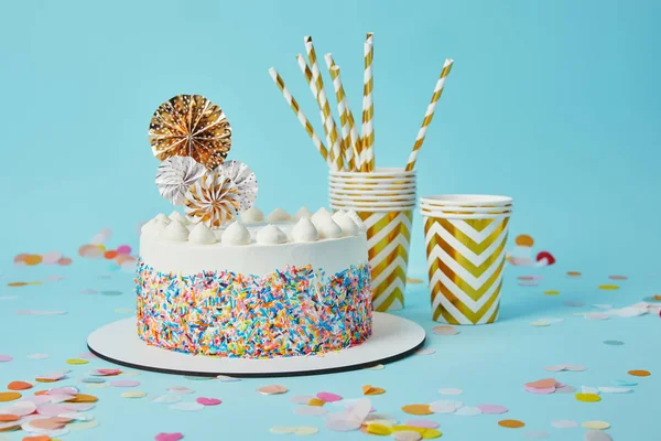 Deliziosa torta, tazze plactiche e cannucce da bere su sfondo blu con coriandoli — Foto stock