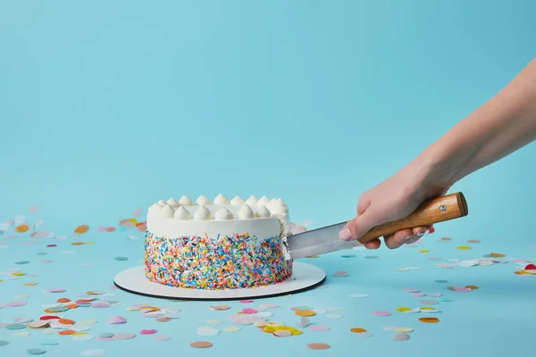 Vue recadrée de la femme coupant délicieux gâteau sur fond bleu — Photo de stock