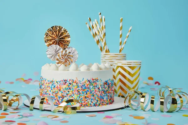 Delicious cake, plactic cups and drinking straws on blue background with confetti — Stock Photo