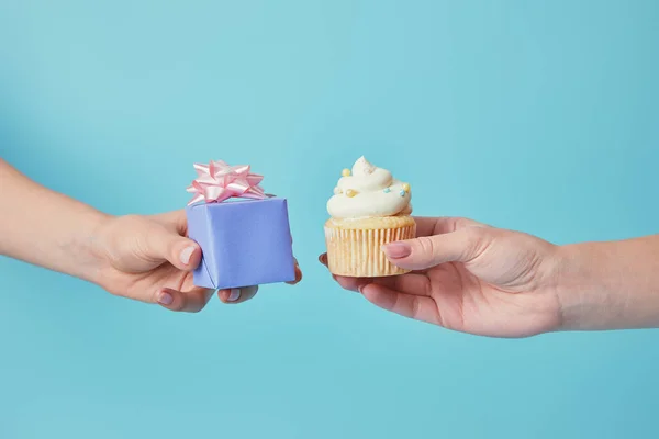 Abgeschnittene Ansicht von Frauen mit leckerem Cupcake und Geschenk auf blauem Hintergrund — Stockfoto
