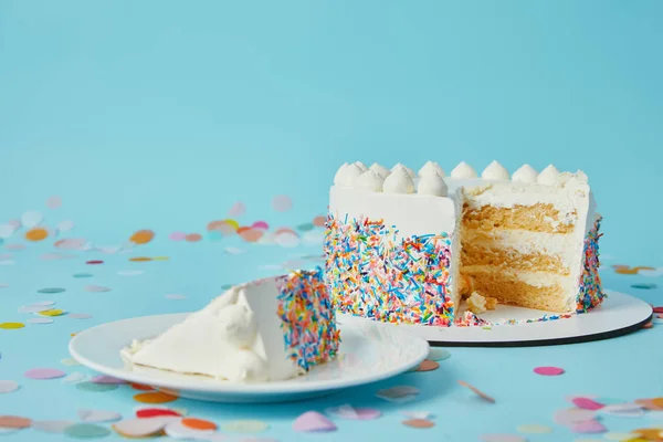 Slice of cake with cut cake on blue background with confetti — Stock Photo