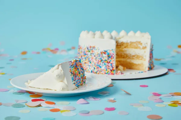 Piece of cake with cut cake on blue background with confetti — Stock Photo