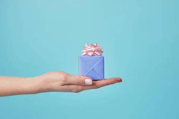 Vista parcial de mujer sosteniendo regalo con lazo rosa sobre fondo azul — Stock Photo