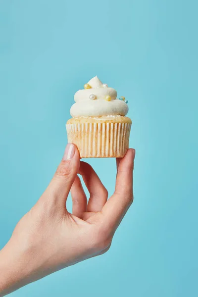 Vista recortada de la mujer sosteniendo delicioso cupcake sobre fondo azul - foto de stock