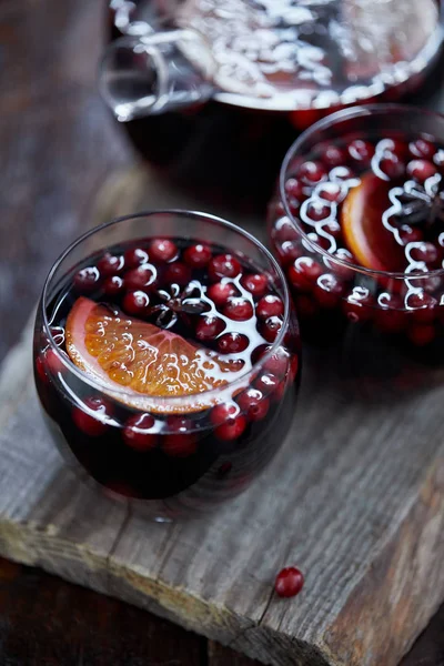 Vista de alto ângulo de copos de vinho ruminado caseiro com cranberries e laranjas em suporte de madeira na cozinha — Fotografia de Stock