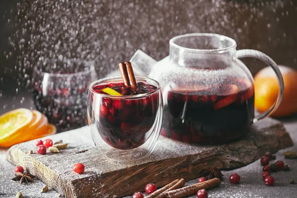 Homemade mulled wine with cranberries in glasses and teapot with falling powdered sugar on table in kitchen — Stock Photo