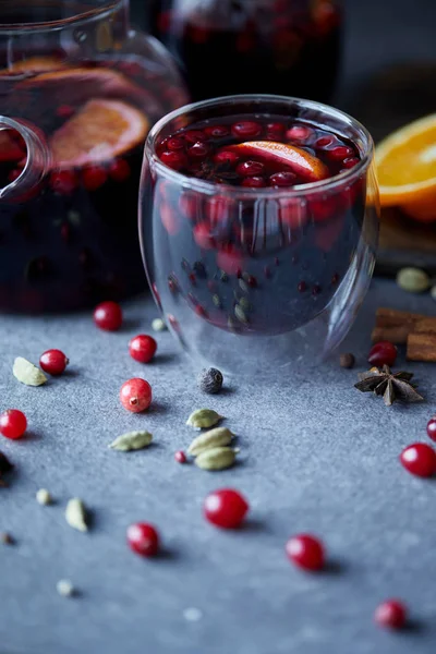 Foco seletivo de vinho quente caseiro saboroso com cranberries e laranjas na mesa na cozinha — Fotografia de Stock
