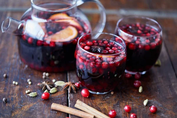 Vino caliente casero con arándanos en copas y tetera sobre mesa de madera en cocina - foto de stock