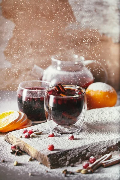 Açúcar em pó caindo em dois copos de vinho ruminado caseiro com cranberries na mesa na cozinha — Fotografia de Stock