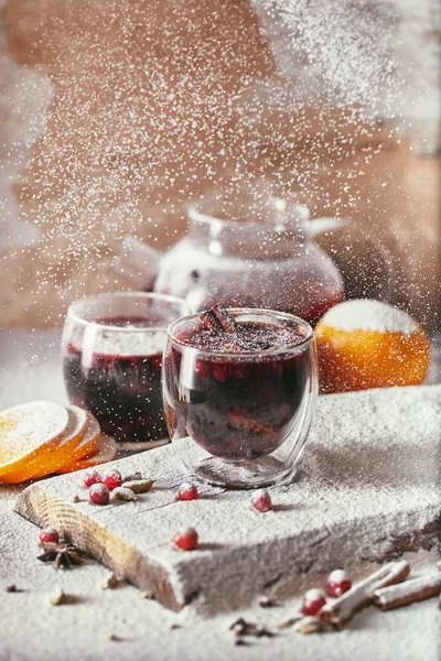 Sucre en poudre tombant sur deux verres de vin chaud savoureux avec des canneberges sur la table dans la cuisine — Photo de stock