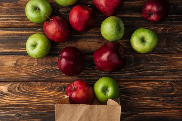 Top view of scattered red and green apples with paper bag on wooden table — Stock Photo