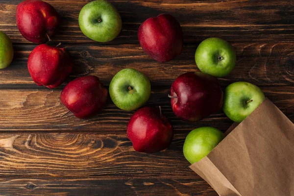 Vista superior de manzanas rojas y verdes maduras con bolsa de papel sobre mesa de madera - foto de stock